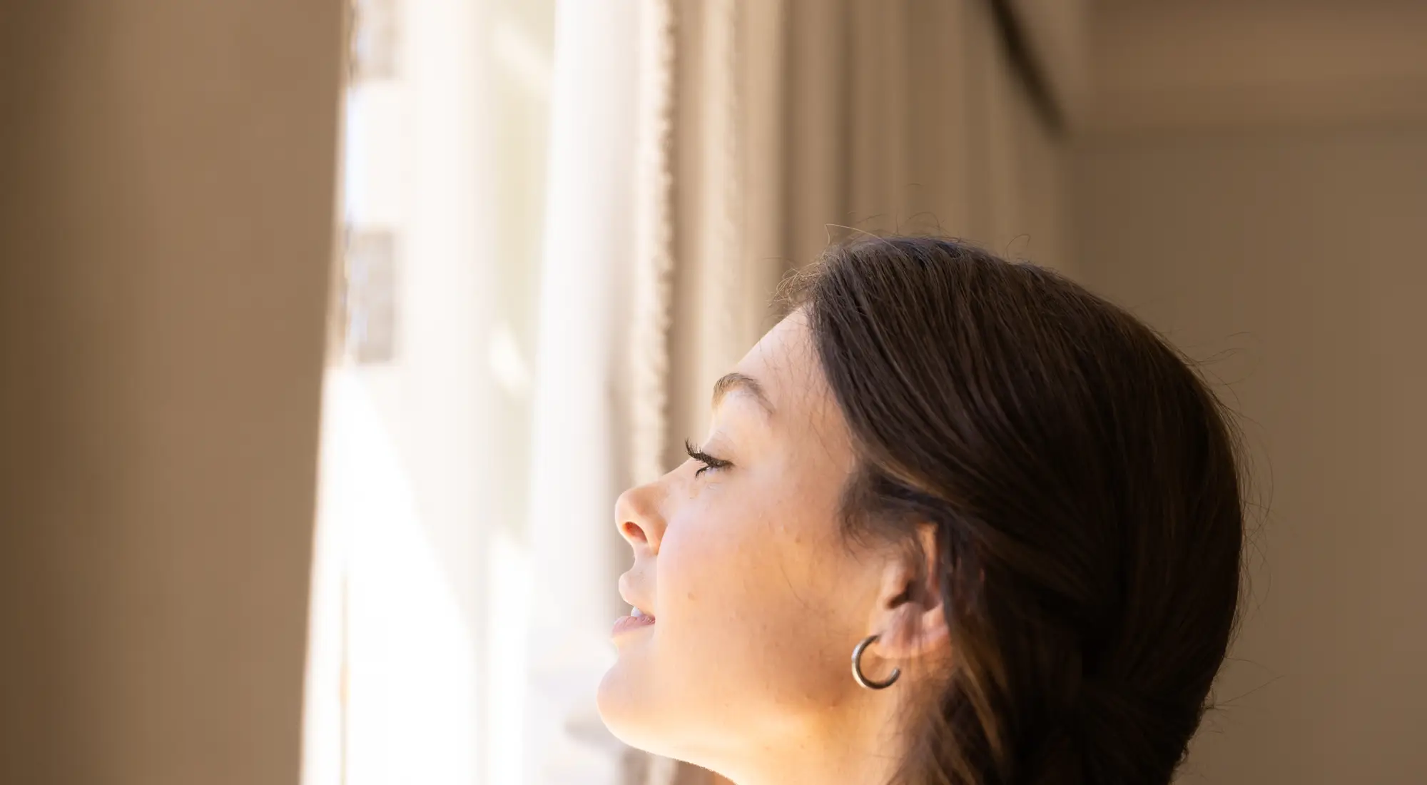A woman gazing out a sunlit window, hopeful