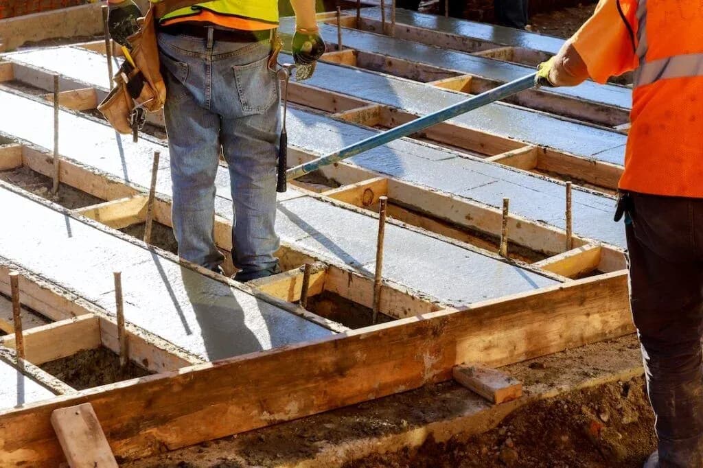 Workers levelling concrete within foundation formwork