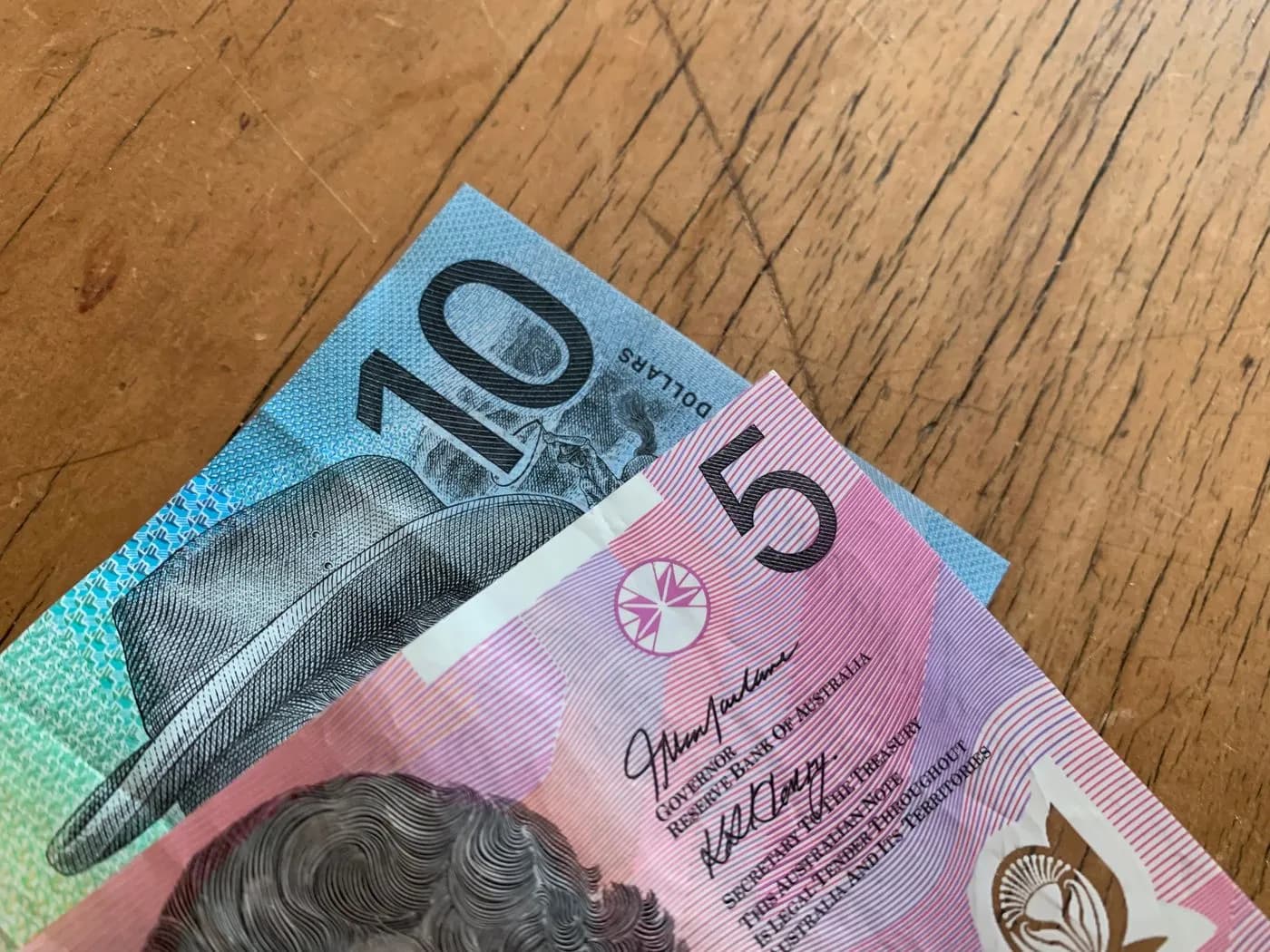 Australian $5 and $10 banknotes on a wooden surface.