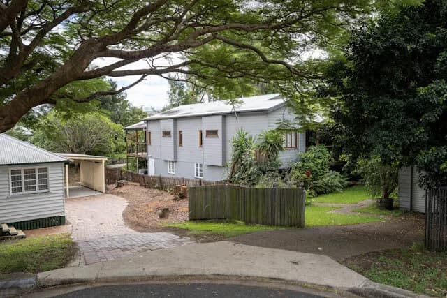 A weatherboard cottage under a large shade tree on a leafy Brisbane street