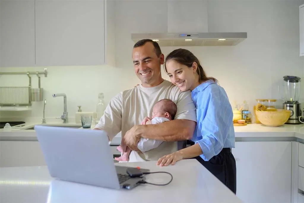 Parents with their newborn reviewing household finances on a laptop