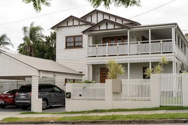 A renovated two-storey timber Queenslander with a wide verandah on a Brisbane street