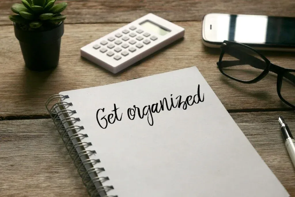 Notebook reading “Get organized” beside a calculator, phone and glasses