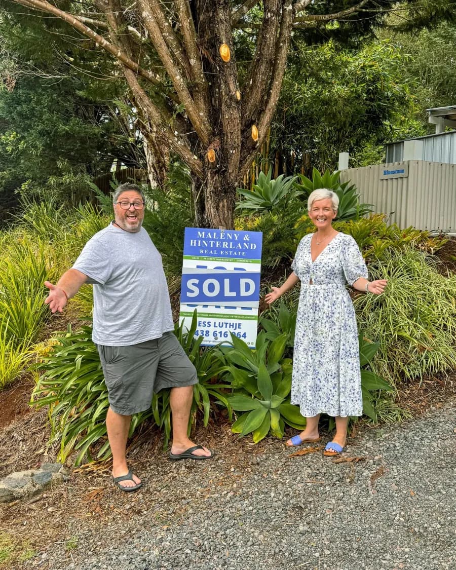 Annie and Steve beside the SOLD sign at the home they bought in the Sunshine Coast Hinterland